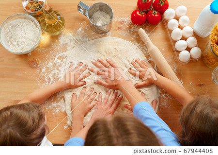 Mother and her kids kneading dough on kitchen table Mother and her kids kneading dough on kitchen table 67944408