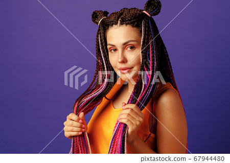 Smiling positive young woman with colorful african braids on purple background Smiling positive young woman with colorful african braids on purple background 67944480