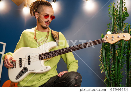 Young fashionable man in pink sunglasses playing guitar with joy 67944484