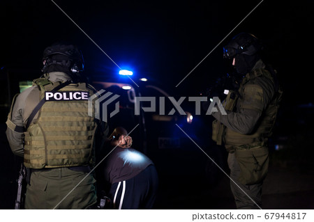 A police officer puts handcuffs on a criminal's hands during an arrest. Police car with flashing lighthouses 67944817