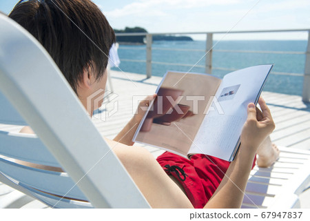 Man sitting on a summer bed and reading a magazine 67947837