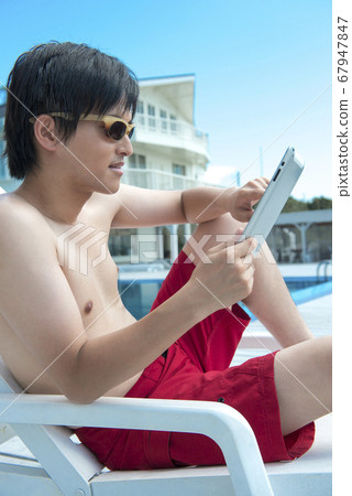 A man sitting on a summer bed and looking at a tablet PC 67947847