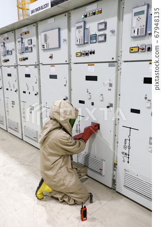 The operator wear arc flash suit, electrical safety gloves and high voltage insulating boots to open power compartment door for rack out circuit breaker form switchgear 67948135