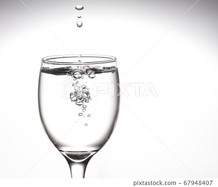 A tall glass, a glass of wine with clear water with bubbles floating in the mouth of the glass Inside 67948407