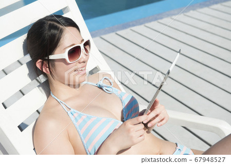A woman in a swimsuit looking at a tablet PC A woman in a swimsuit looking at a tablet PC 67948527