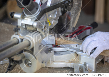Carpenter cuts a timber beam with a circular saw. A closeup of hands in gloves. Carpenter cuts a timber beam with a circular saw. A closeup of hands in gloves. 67949752