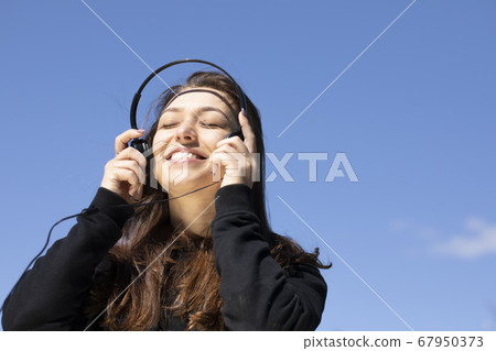 Happy woman with beautiful smile puts on headphones listening summer music Happy woman with beautiful smile puts on headphones listening summer music 67950373