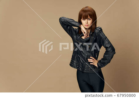 Young beautiful woman posing on a beige background in the studio in a black leather jacket 67950800