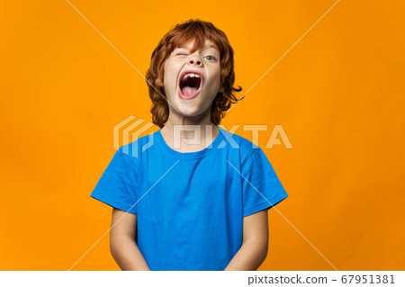 An emotional child with a wide open mouth yawns blue t-shirt yellow background red hair An emotional child with a wide open mouth yawns blue t-shirt yellow background red hair 67951381