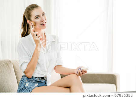 Beautiful woman use cosmetics and sit on sofa and look to camera in living room Beautiful woman use cosmetics and sit on sofa and look to camera in living room 67955393