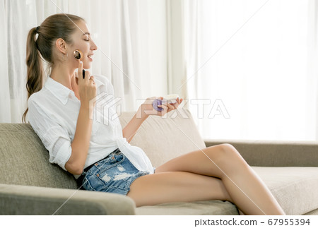 Beautiful woman use cosmetics and sit on sofa in living room of her house with morning light 67955394