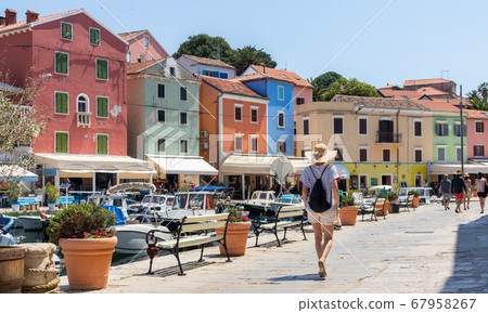 Rear view of beautiful blonde young female traveler wearing straw sun hat sightseeing and enjoying summer vacation in an old traditional costal town of Veli Losinj, Adriatic cost, Croatia Rear view of beautiful blonde young female traveler wearing straw sun hat sightseeing and enjoying summer vacation in an old traditional costal town of Veli Losinj, Adriatic cost, Croatia 67958267