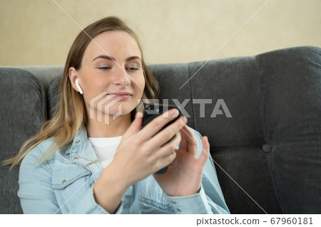 Young woman sitting listening to music with earphones on her mobile phone at home as she relaxes on a sofa. Young woman sitting listening to music with earphones on her mobile phone at home as she relaxes on a sofa. 67960181