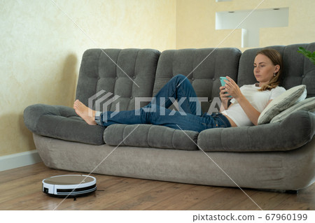 Attractive girl using smartphone while robotic vacuum cleaner cleaning house Attractive girl using smartphone while robotic vacuum cleaner cleaning house 67960199