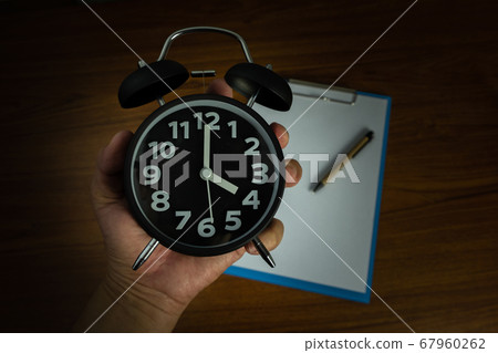 Black vintage alarm clock in hand with clipboard Black vintage alarm clock in hand with clipboard 67960262