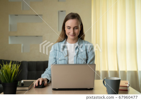 Beautiful young woman working on laptop computer while sitting at the living room 67960477
