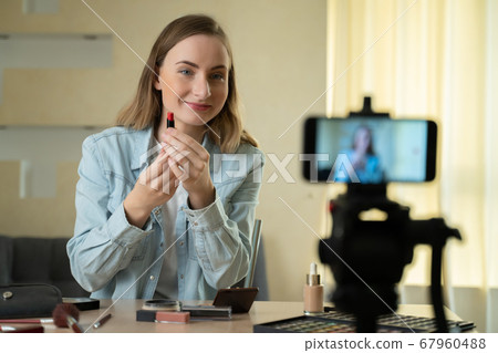 Beauty blogger woman filming make-up tutorial on camera. Influencer woman live streaming cosmetics product review in home studio Beauty blogger woman filming make-up tutorial on camera. Influencer woman live streaming cosmetics product review in home studio 67960488