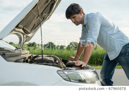 Man standing next to a broke down car, looking down at engine in frustration 67960878