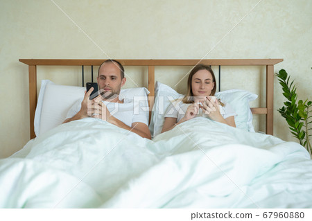 Couple lying in bed using mobile phone while ignoring each other. Man and woman addicted to smartphone social networks technology. 67960880