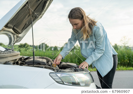 Woman standing near the broken car. The girl opened the hood and look at the engine. Woman standing near the broken car. The girl opened the hood and look at the engine. 67960907