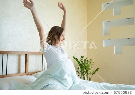 Woman waking up in her bed fully rested. Woman stretching in bed after wake up. Woman waking up in her bed fully rested. Woman stretching in bed after wake up. 67960988