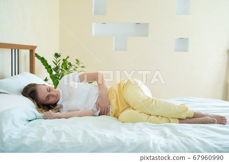 Woman suffering from abdominal pain while lying on bed at home 67960990