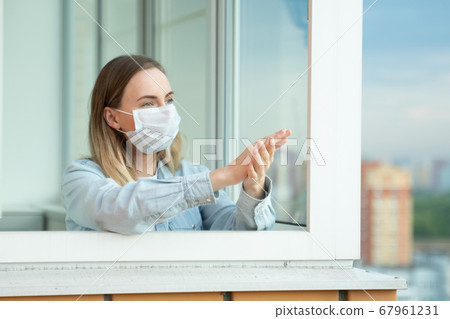 Woman applauds on the balcony of her apartment, thanking the medical services for Covid-19. 67961231