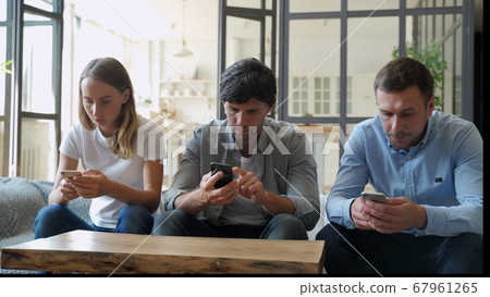 Group of three friends hanging out but ignoring each other while using their smartphones at home 67961265