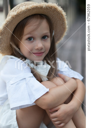 a little girl in a hat looks at the camera with her hand held to her face a little girl in a hat looks at the camera with her hand held to her face 67962059