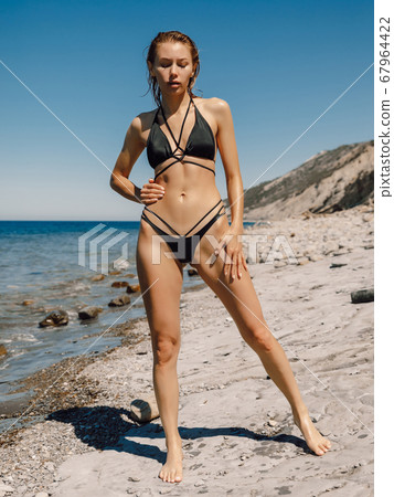 Sexy slim woman in bikini posing at sea beach. Attractive model with sporty body 67964422