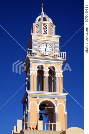 St John the Baptist Cathedral is a Roman Catholic church in Fira (Thira), Santorini, Greece.  It is one of many churches in Fira, Santorini.  The church has a clock tower against a blue sky. Santorini 67968412