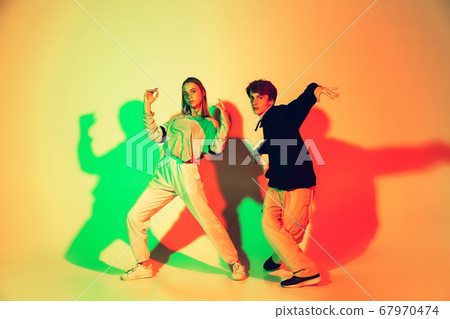 Young man and woman dancing hip-hop, street style isolated on studio background in neon light 67970474