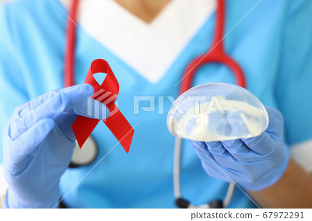 Doctor holds breast implant and red ribbon in his hand. Doctor holds breast implant and red ribbon in his hand. 67972291