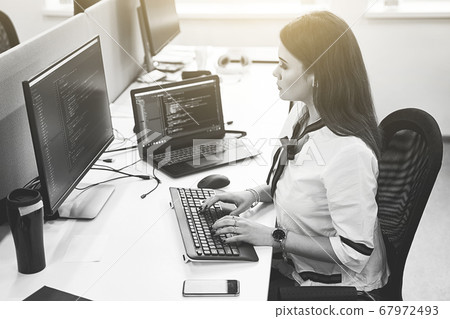 Beautiful female software developer working on computer in IT office, sitting at desk and coding, working on a project in software development company or technology startup. Black and white, Beautiful female software developer working on computer in IT office, sitting at desk and coding, working on a project in software development company or technology startup. Black and white, 67972493