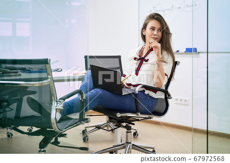 Beautiful female junior software developer working on laptop in IT office, sitting at table in meeting room of a software development company or technology startup. High quality image. 67972568