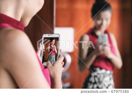 Mirror selfie woman taking picture with mobile phone in store mirror shopping for clothes looking at her fashion oufit for office taking selfies in changing room. Weight loss, body image, self-esteem. 67975380