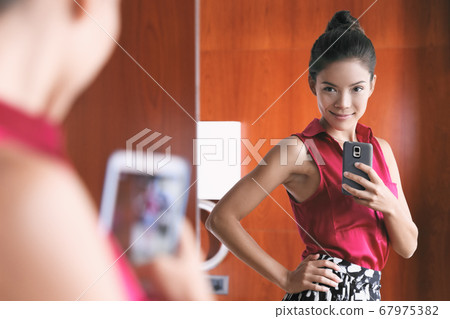 Mirror selfie confident Asian woman feeling pretty good in her body self-esteem taking photo with mobile phone in home closet looking at her slim weight loss waistline. 67975382