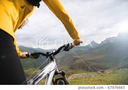A close-up of the girl's hand cyclist on the handlebars of a mountain bike against the backdrop of epic rocks and mountains. Mountain bike. Girls cyclist 67976665