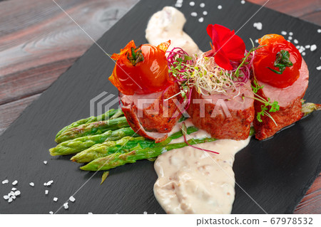 veal medallions with asparagus on black dishware , wooden table 67978532