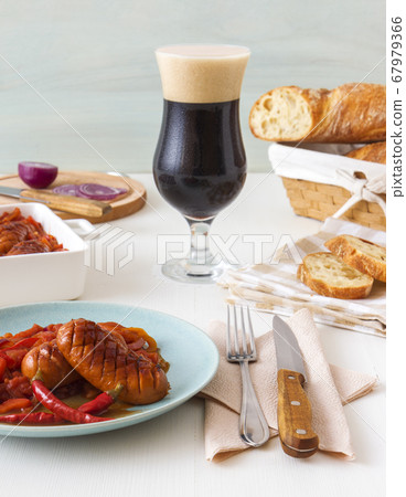 Baked sausages in dark beer with red onion, red and yellow paprika, bread and glass of dark beer. Baked sausages in dark beer with red onion, red and yellow paprika, bread and glass of dark beer. 67979366