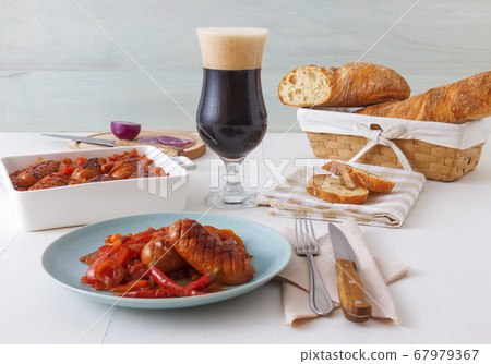 Baked sausages in dark beer with red onion, red and yellow paprika, bread and glass of dark beer. Baked sausages in dark beer with red onion, red and yellow paprika, bread and glass of dark beer. 67979367