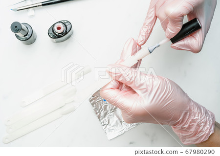Manicurist at work in the office. Drawing gel polish on tips, creating a picture. Equipment and inventory of a manicure cabinet. 67980290