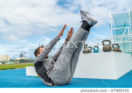 Abs exercise leg lift toe touch sit-up workout man strength training at fitness gym athletic stadium. Athlete working out crunches exercises for stomach muscles and weight loss. 67980430