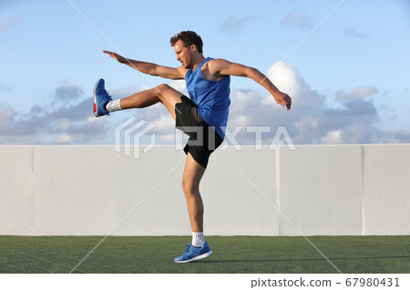 Runner man getting ready to run doing warm-up dynamic leg stretch exercises routine, Male athlete stretching lower body hamstring muscles before going running outside in summer outdoors. Runner man getting ready to run doing warm-up dynamic leg stretch exercises routine, Male athlete stretching lower body hamstring muscles before going running outside in summer outdoors. 67980431