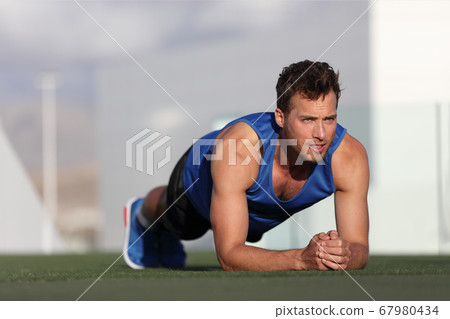Crossfit training fitness man doing plank core exercise working out his midsection core muscles. Fit male fitness instructor planking exercising outside in summer park grass. Outdoor stadium. 67980434