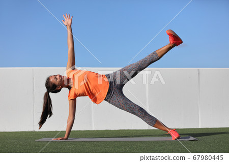 Star Side Plank. Yoga woman planking doing leg lift core exercise at fitness gym class. Asian girl training side plank leg raise body core in yoga studio on home outdoor grass. Fitness gym lifestyle. Star Side Plank. Yoga woman planking doing leg lift core exercise at fitness gym class. Asian girl training side plank leg raise body core in yoga studio on home outdoor grass. Fitness gym lifestyle. 67980445