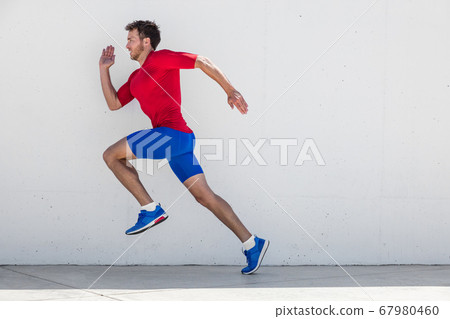 Running man runner training doing outdoor city run sprinting along wall background. Urban healthy active lifestyle. Male athlete doing sprint hiit high intensity interval training. 67980460