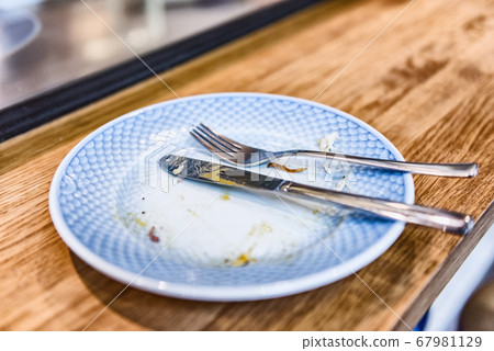 Empty plate after finished meal at restaurant - fork and knife resting on done dinner with crumbs at bistro counter. Empty plate after finished meal at restaurant - fork and knife resting on done dinner with crumbs at bistro counter. 67981129