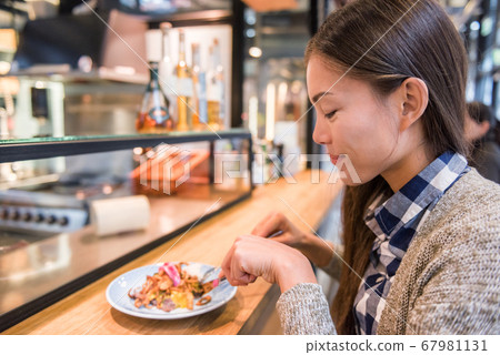 Woman eating at danish restaurant the traditional smorrebrod open sandwich at market stall counter. Happy Asian tourist trying typical meal from Denmark. Copenhagen city travel lifestyle. Woman eating at danish restaurant the traditional smorrebrod open sandwich at market stall counter. Happy Asian tourist trying typical meal from Denmark. Copenhagen city travel lifestyle. 67981131