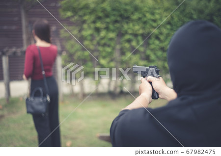 bandit using black gun point to backward of woman, concept of criminal, bandit, gangster, mafia bandit using black gun point to backward of woman, concept of criminal, bandit, gangster, mafia 67982475